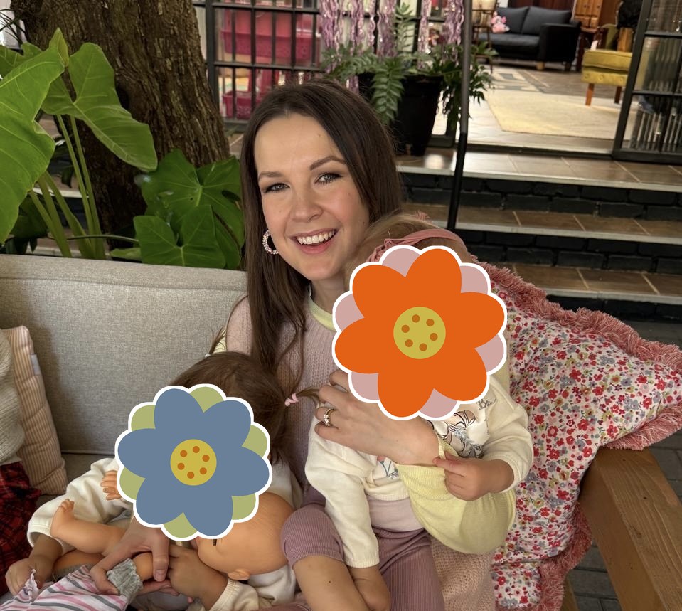 Linki Raubenheimer smiling on a garden bench with her two young children, their faces covered by painted flowers